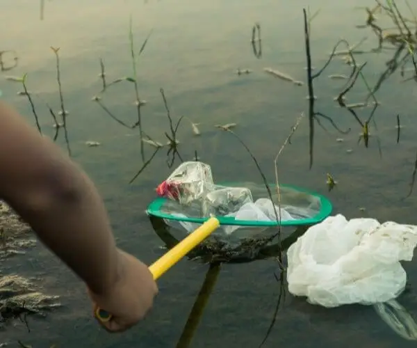 child doing volunteer work by cleaning plastic from a lake