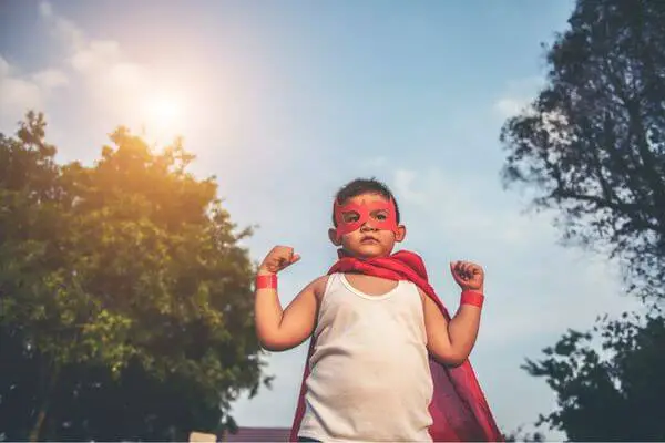 little boy with a red cape and red mask in a superhero pose